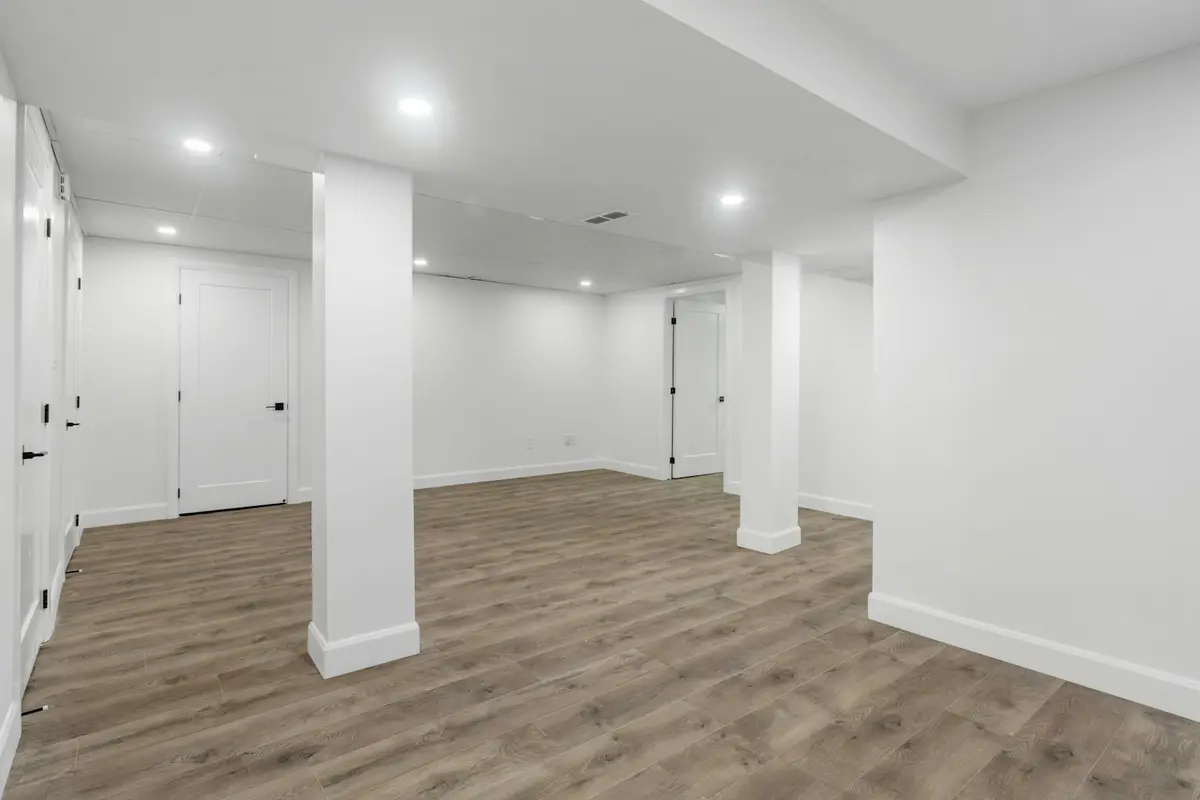 A bright finished basement with a support column and plank flooring