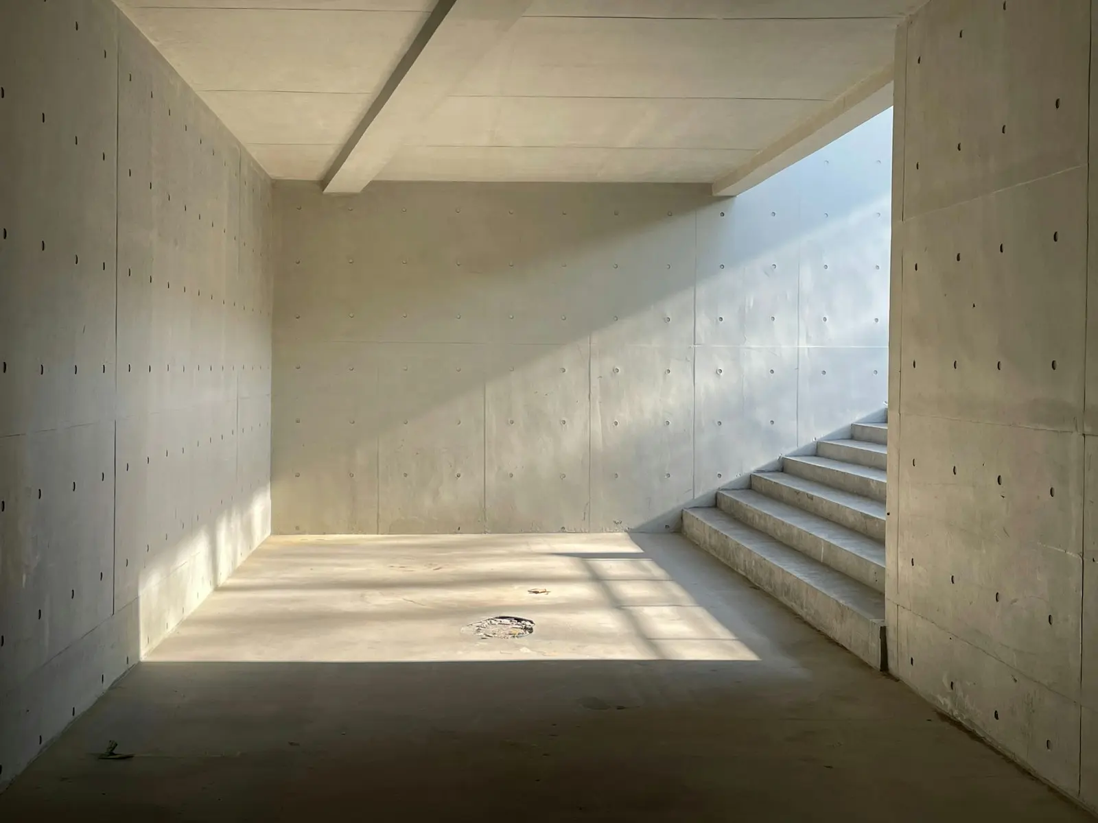 A raw concrete basement room with daylight down the stairs