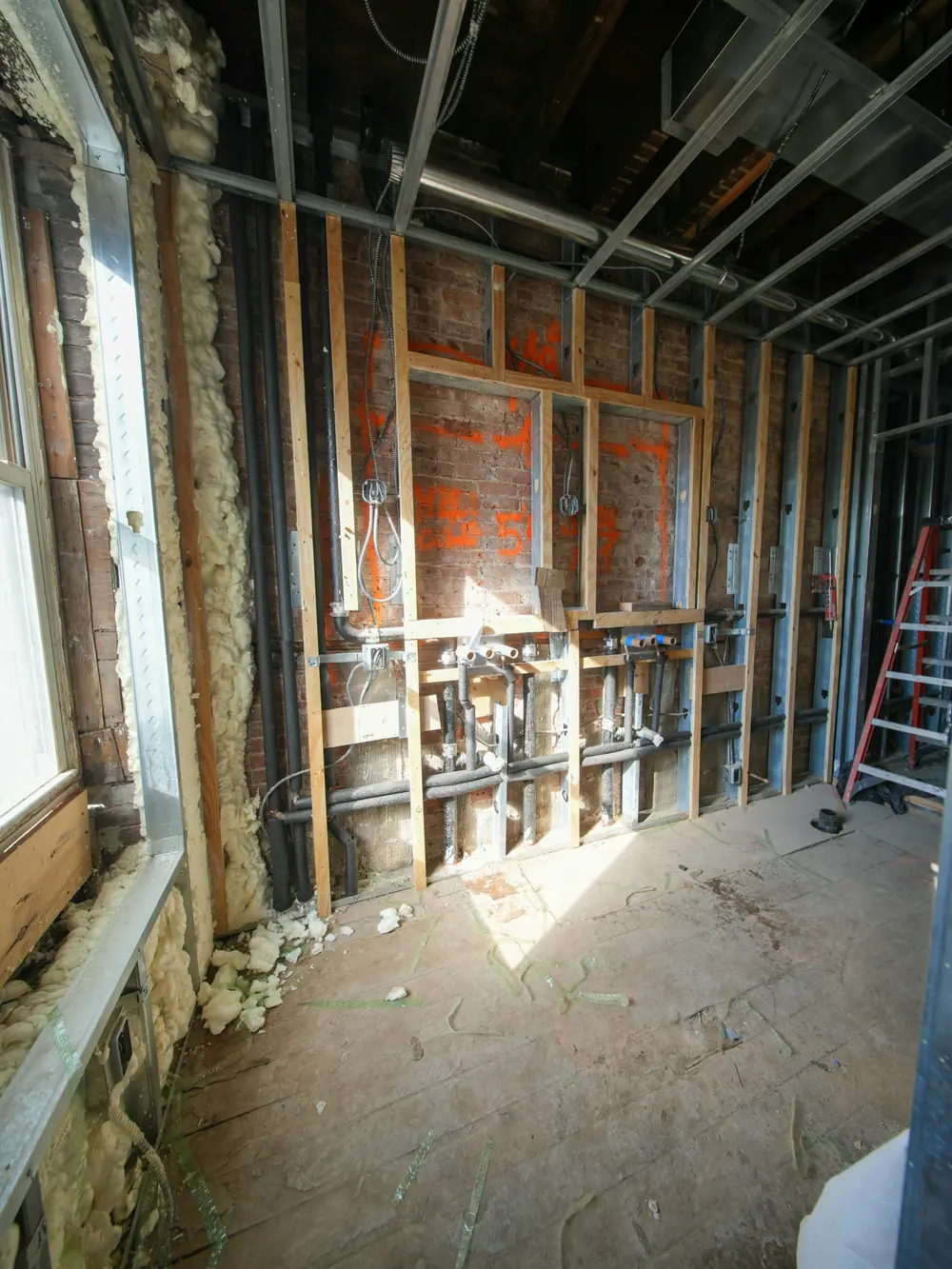 New plumbing and electrical rough-in against an exposed brick basement wall